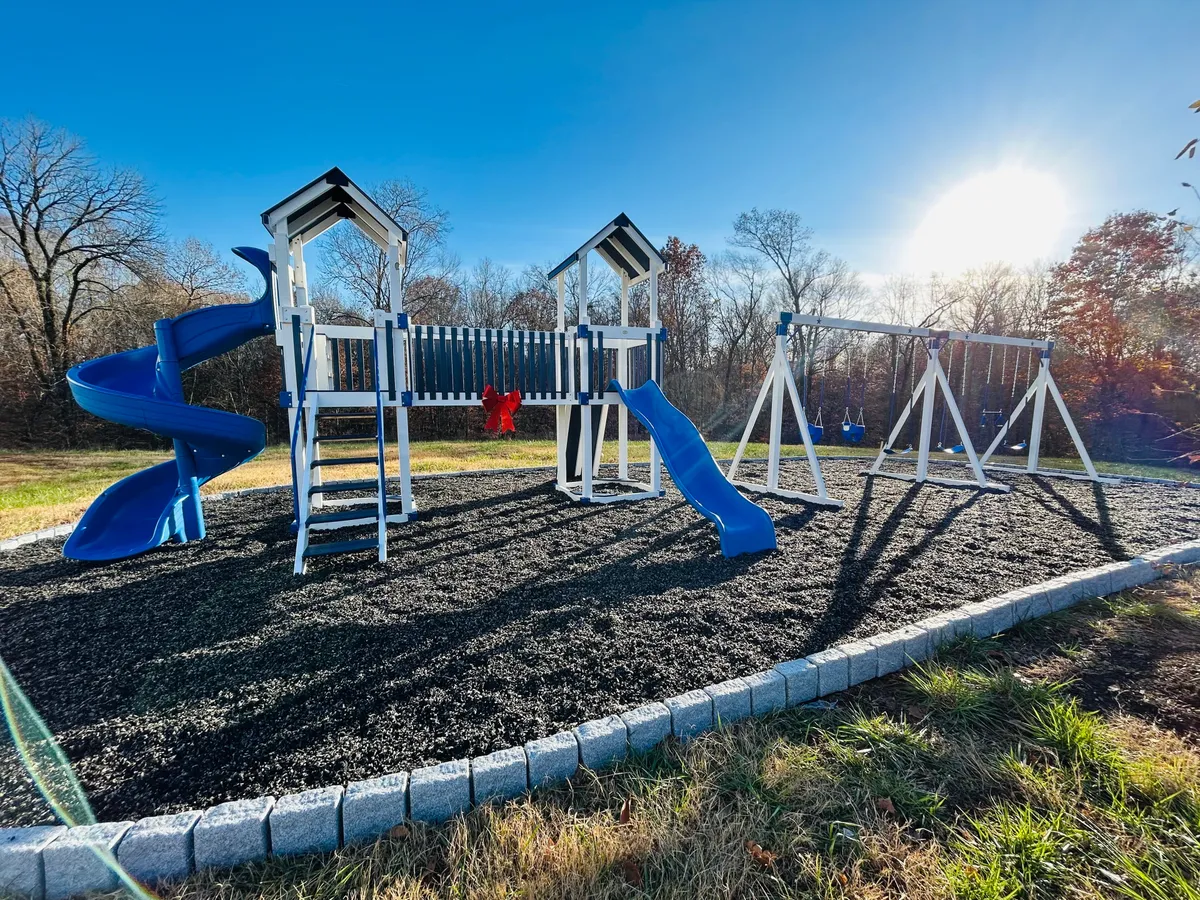 This exterior image features a vibrant playground with equipment such as a slide and swings, set against a green outdoor backdrop. Children are shown at play, and the area is designed for family gatherings and outdoor fun, conveying a joyful, communal atmosphere.