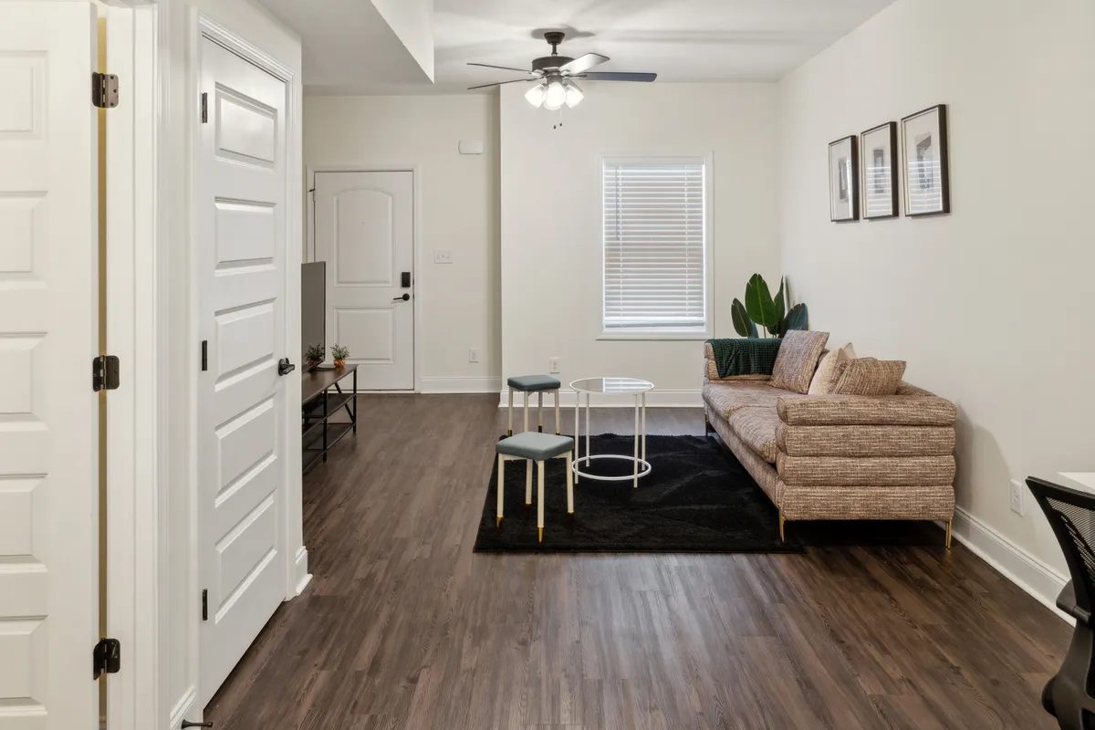 A cozy living area featuring a sofa, coffee table, potted plant, and wall art. The setup is perfect for relaxing, hosting small gatherings, or enjoying quiet moments with a book.