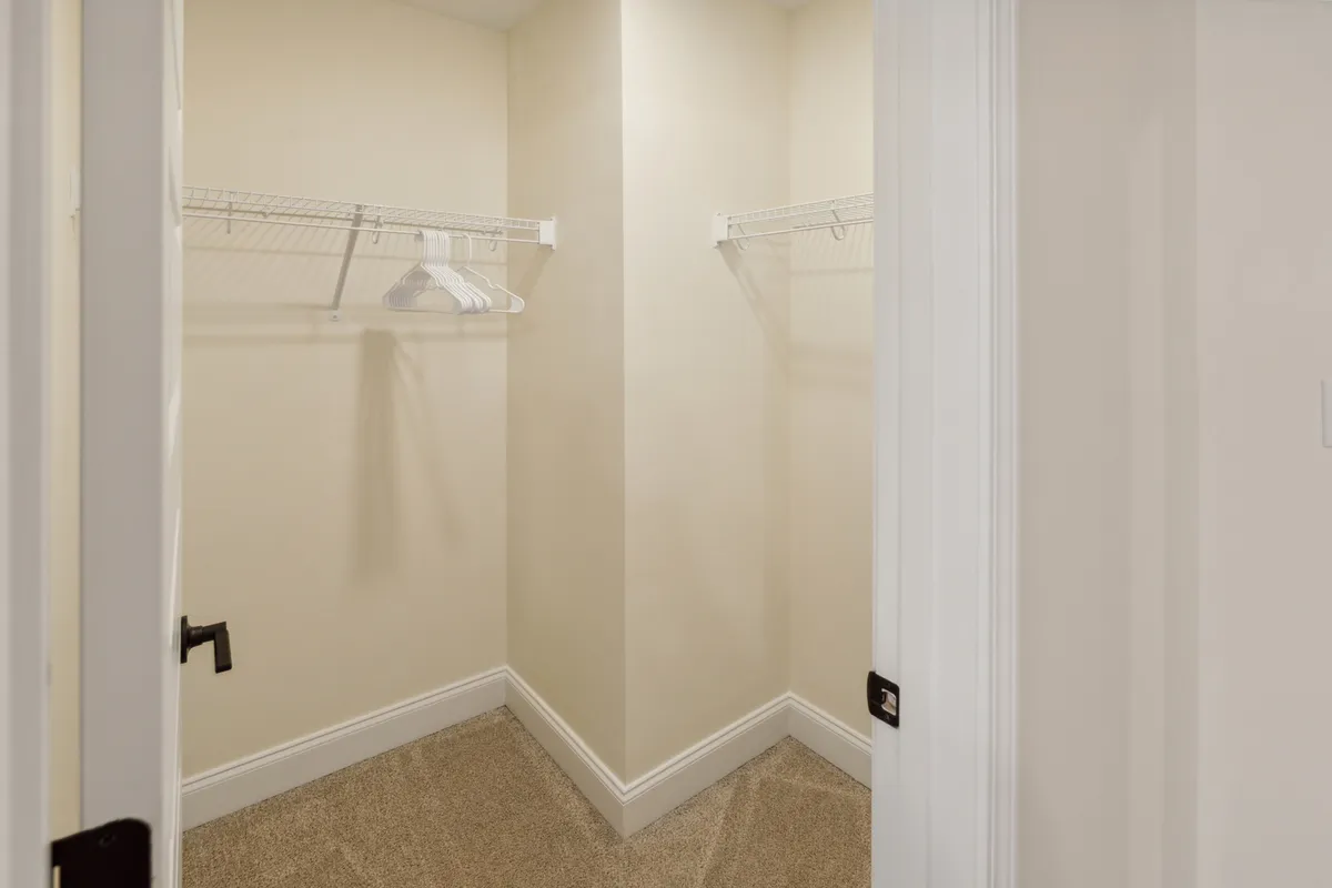 A spacious closet with wire shelving, carpeted flooring, and clean white walls. The area is uncluttered and bright, ready for organizing clothes and personal belongings.