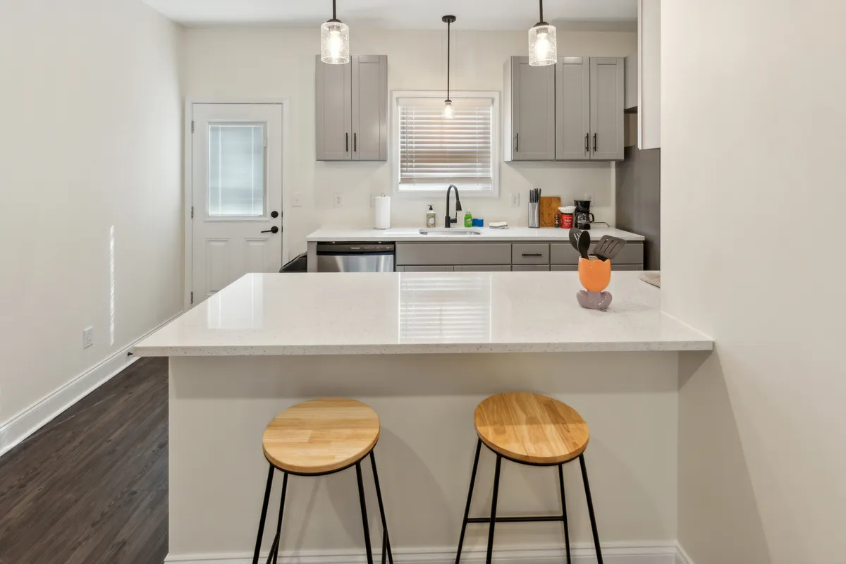 A stylish kitchen featuring a kitchen island with stools, contemporary appliances, and thoughtful countertop decor. The open seating invites casual dining or gathering with friends and family, creating an atmosphere ideal for shared meals and lively conversation.