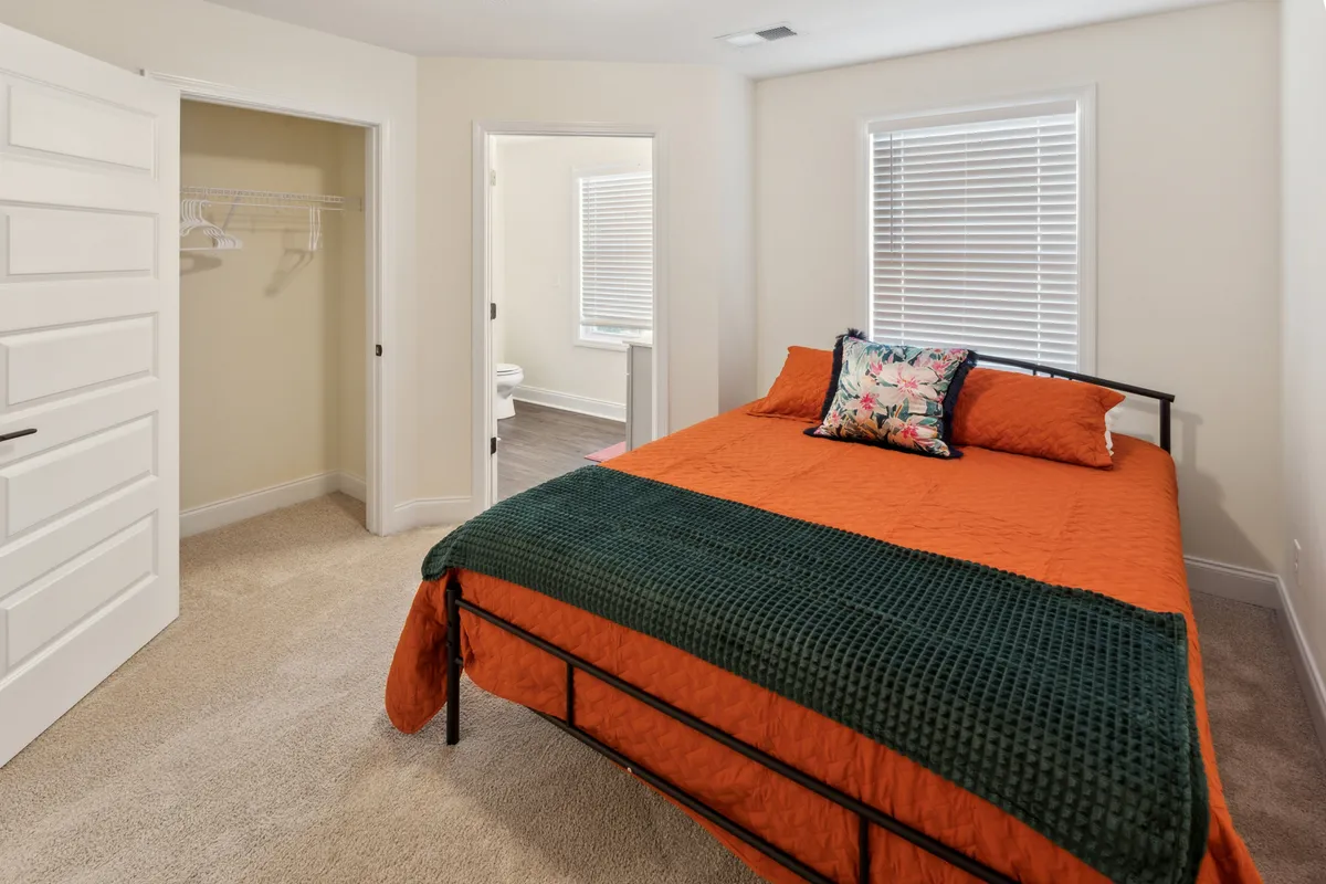 A tranquil bedroom with a comfortable bed made up with decorative pillows, soft bedding, and sunlight gently filtering through large windows. The space exudes relaxation, inviting a restful night's sleep or a quiet moment for reading.