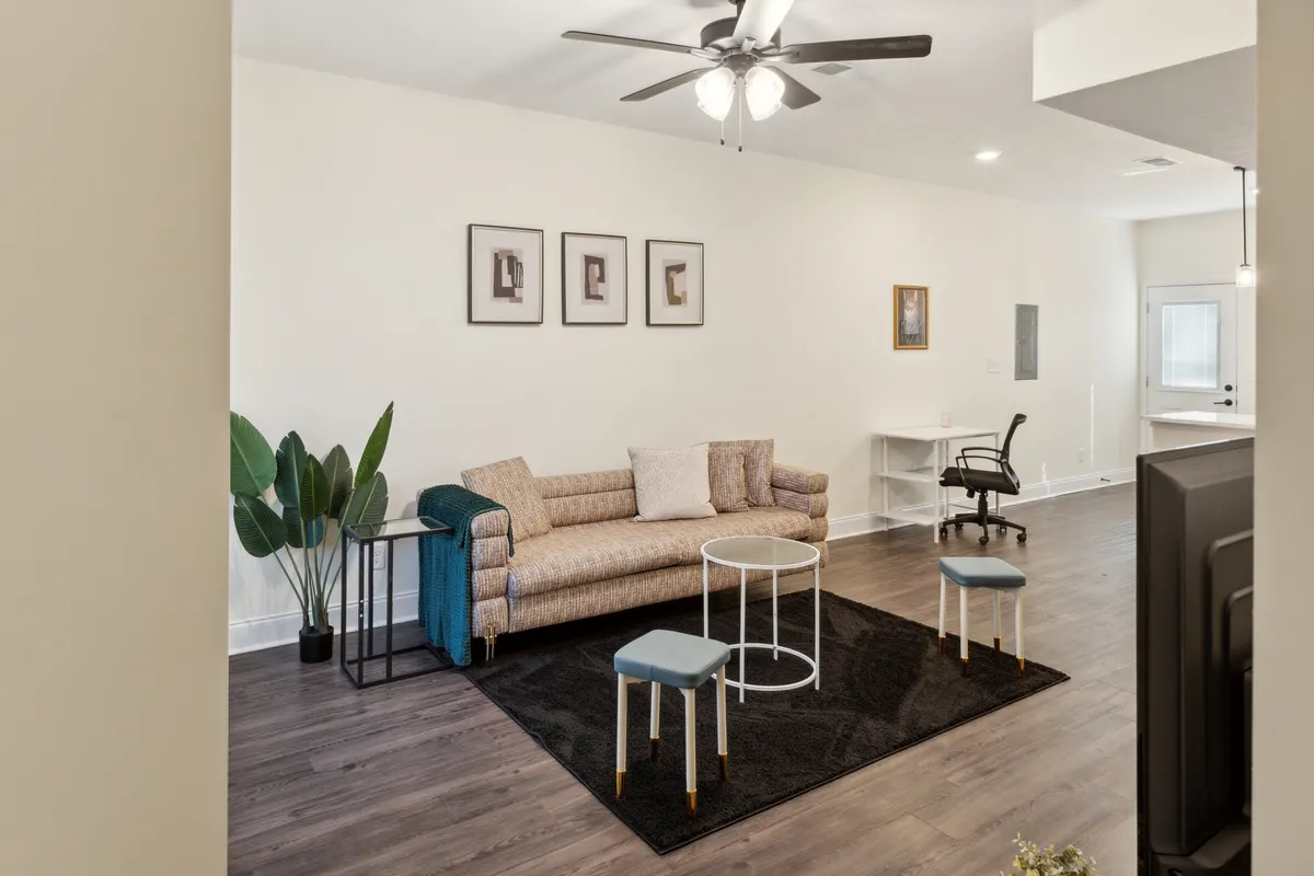 The image showcases a stylish apartment living area, featuring an inviting sofa, a modern coffee table, vibrant artwork on the walls, and touches of greenery from potted plants. The space is bright and open, exuding a comfortable, welcoming vibe ideal for both relaxation and gathering with loved ones.