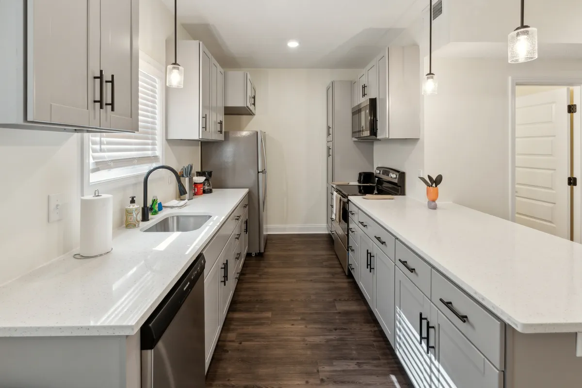 This image features a welcoming kitchen with a countertop, sink, modern appliances, and inviting lighting fixtures. The scene suggests opportunities for families to gather and connect over meals after a day out. The kitchen appears spacious and practical for preparing snacks or dinners, evoking a sense of togetherness.